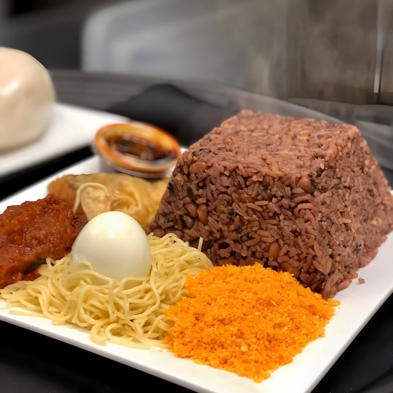 A plate of Accra Girls Restaurant's African food, including rice, noodles, egg, and sauces.