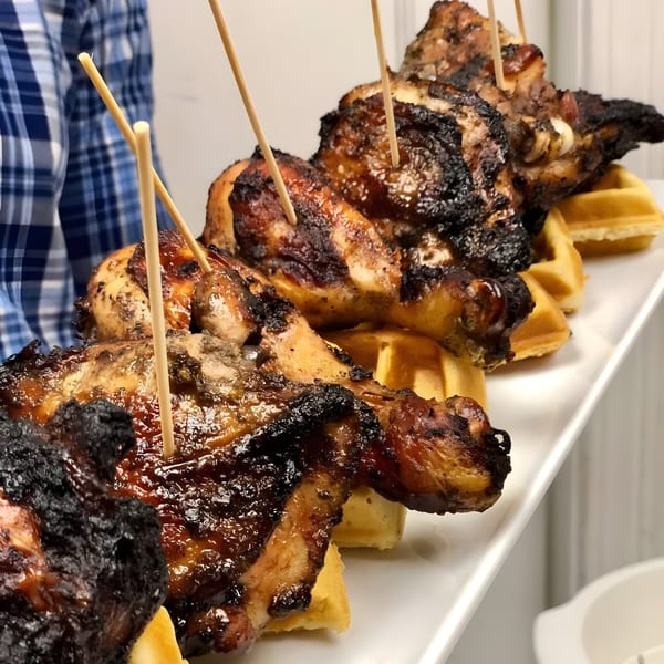 Grilled chicken pieces with crispy skin and toothpicks, served on waffles on a white platter.