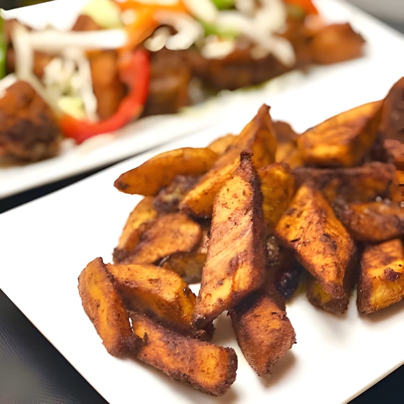 Crispy fried plantain slices, known as kelewele, on a white plate at Accra Girls Restaurant.