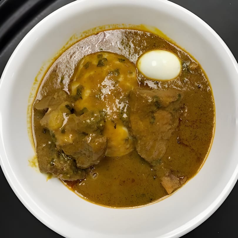 African fufu with chicken and egg in a rich, savory stew, served in a white bowl.