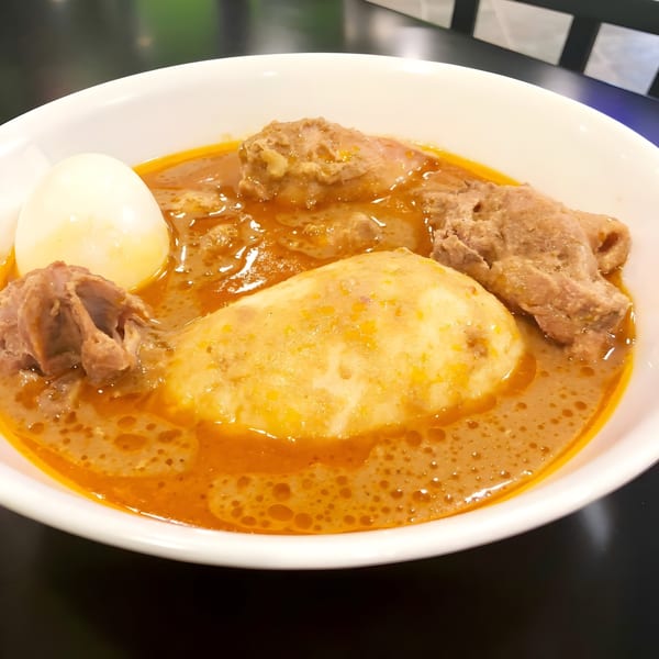 Accra Girls Restaurant's fufu with chicken, egg, and a rich, orange-brown soup in a white bowl.