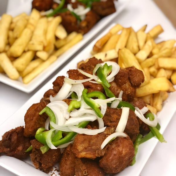 Two plates of Accra Girls Restaurant's fried chicken with onions, green peppers, and french fries.